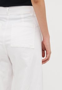 Pantalones de algodón blancos con una textura suave, que cuentan con dos bolsillos parche en la parte posterior y un diseño de pierna recta.