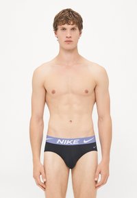 Black briefs with a light purple elastic waistband featuring the Nike logo in white. Material appears smooth and fitted.