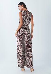 Ärmelloser Jumpsuit mit einem braun- und cremefarbenen Zebra-Muster, der eine taillierte Taille, ein weit geschnittenes Bein und ein kleines Schlitzdetail auf dem Rücken aufweist.