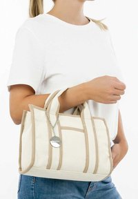 Borsa in tela beige con accenti crema, dotata di due manici robusti, chiusura con zip e un dettaglio di portachiavi con etichetta rotonda.