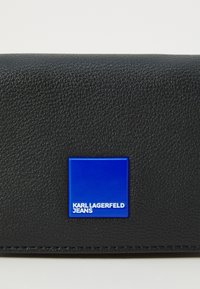 Portafoglio nero con texture, dotato di una patch rettangolare blu liscia che mostra la scritta "KARL LAGERFELD JEANS" in bianco, con un design minimalista.