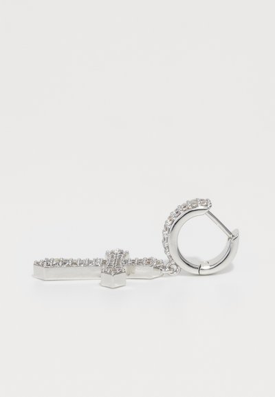 Boucles d'oreilles en argent avec un pendentif en croix suspendu orné de petites cristaux ronds sur un fond blanc uni.