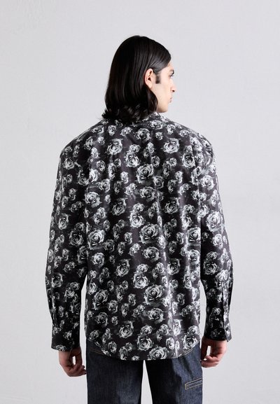 Black shirt featuring a white floral pattern, long sleeves, and a loose fit. The fabric appears smooth with a slight sheen.