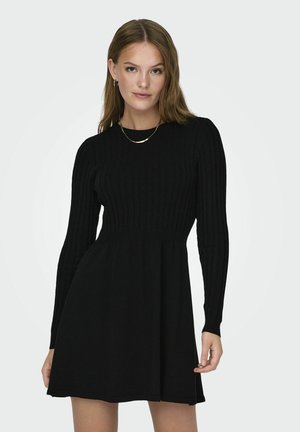 Black ribbed long-sleeve dress with a fitted bodice and flared skirt, made from soft material. Golden necklace as an accessory.