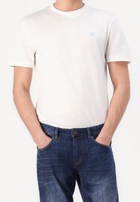 Vit t-shirt i bomull med rund hals och korta ärmar, med en liten blå logotyp. Matchad med mörkblå denimjeans med knäppning.