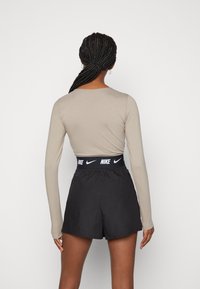 Abbigliamento sportivo Nike da donna caratterizzato da una maglietta beige a maniche lunghe e pantaloni corti neri con un cinturino bianco con logo. Tessuto liscio, design aderente.