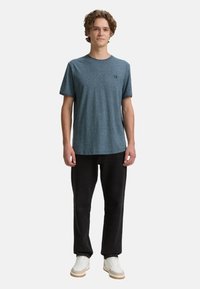 Rövid ujjú, kék heather póló, puha, könnyű anyagból készült. Fekete nadrággal és fehér sportcipővel párosítva, diszkrét logóval.