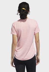 Kortärmad rosa träningströja med rundad nederkant, gjord av lättviktigt material. Slät textur, bärs med svarta leggings.