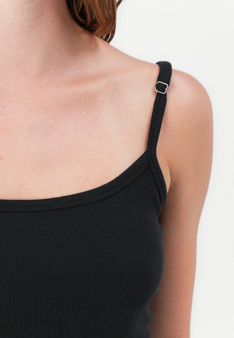 Czarny prążkowany top na ramiączkach z cienkimi paskami i srebrnymi akcentami. Charakteryzuje się okrągłym dekoltem i dopasowanym krojem.