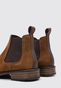 Botas Chelsea de ante marrón con paneles laterales elásticos y lengüetas, con tacón apilado y suela de goma texturizada.