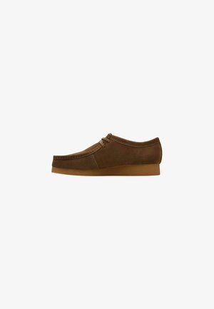 Scarpa in suede marrone con punta arrotondata, cuciture minime e due occhielli per i lacci. Presenta una suola in gomma e un'altezza media.