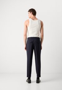 White ribbed tank top paired with navy trousers featuring rolled cuffs and two rear pockets. Black shoes complete the outfit.