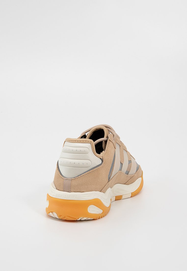Beige Wildledersneaker mit grauen Akzenten, strukturierten Seitenpaneelen und einer klobigen orangen Gummisohle. Verfügt über eine gepolsterte Ferse und Logodetails.