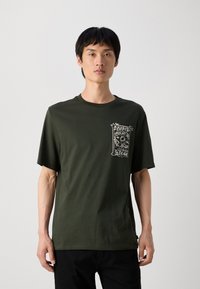 Mørkegrøn bomulds t-shirt med kortærmer, rund halsudskæring og et hvidt grafisk print på venstre brystlommeområde.