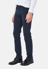 Pantaloni aderenti blu navy realizzati in tessuto misto cotone. Caratterizzati da una cucitura sottile, tasche anteriori e una texture liscia. Abbinati a scarpe nere.