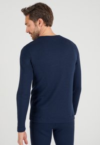 Donkerblauwe gebreide shirt met lange mouwen, een ronde hals en aansluitende manchetten, met een gladde textuur en minimale naden.
