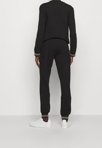 Svart outfit bestående av en långärmad topp och joggers. Har manschetter med gulddetaljer och en avslappnad passform. Vita sneakers fulländar looken.