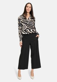 Blouse à motifs noir et crème avec un col, manches longues, associée à un pantalon large noir et des talons clairs.