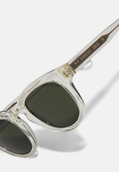 Óculos de sol com armação transparente e lentes verde-escuras. Apresenta acabamentos em tom dourado e gravação da marca na haste. Design angular.
