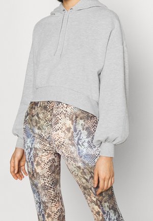 Person iført en lysegrå cropped hættetrøje med snore og højttaljede leggings med et flerfarvet slipskinds-mønster.