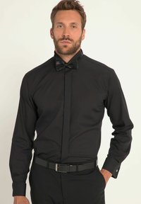 Zwarte formele shirt met hoge kraag en een zwarte strik. Heeft een zachte textuur en lange mouwen met knoopmanchetten, gecombineerd met een zwarte riem.
