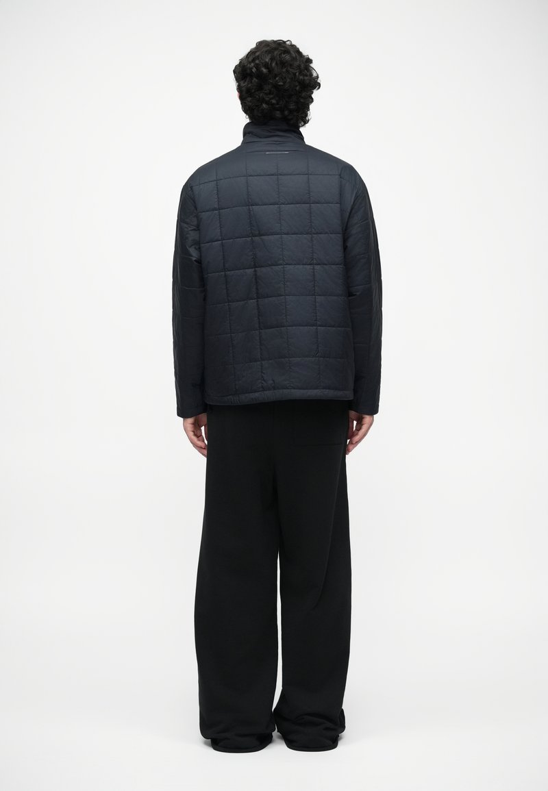 Black, quilted jacket with a stand collar, featuring a boxy fit and side vents. The fabric appears smooth and durable.