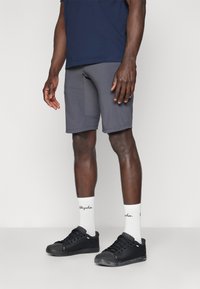Graue Sportshorts mit glatter Textur, kombiniert mit schwarzen Sneakers und weißen Socken. Kurze Länge und enganliegendes Design. Schlichter, einfacher Stil.
