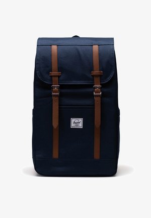 Laadukas tummansininen kangaskäsilaukku, jossa on ruskeat nahkahihnat, varustettu läppäpäällyksellä, säädettävillä hihnoilla ja pienellä logopatchilla edessä.