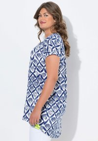 Tunique à manches courtes en blanc et marine, présentant un motif de coquillage. Tissu doux avec une coupe décontractée et des fentes sur les côtés pour plus de mouvement.