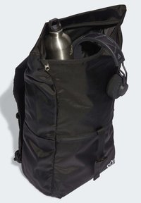 Svart ryggsäck med framfickafack, metallvattenflaska inuti och svarta trådlösa hörlurar hängande på sidan.