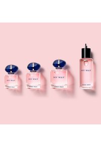 Vier Flaschen Giorgio Armani My Way Parfum vor einem pinkfarbenen Hintergrund, drei mit blauen Kappen und eine mit einem schwarzen Pumpspender.