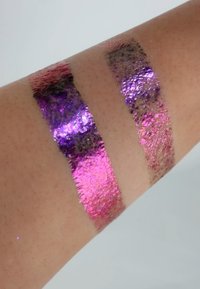 Drei schimmernde Metallfarbproben auf der Haut: ein lebhaftes Fuchsia, ein tiefes Lila und ein Bronze. Glatte Textur mit glitzernden Akzenten.