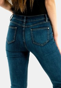 Vaqueros de mezclilla azul oscuro con un diseño ajustado, bolsillos traseros estándar y una textura suave con detalles de costura sutiles.