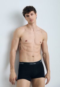 Zwarte katoenen boxershorts met een contrasterende zwart-witte Calvin Klein tailleband, gedragen door een mannelijke model met een atletisch lichaam.