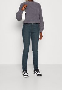 Tmavě modré skinny džíny, texturovaný šedý pletený svetr, bílá kabelka a černo-bílé tenisky. Přiléhavý design s jednoduchým stylem.