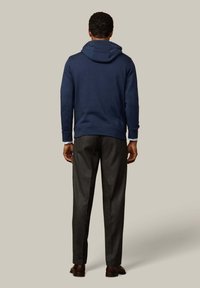 Sudadera navy con capucha ajustable, combinada con pantalones grises. La tela parece suave; los pantalones tienen un corte a medida. Se aprecian contrastes y texturas sutiles.