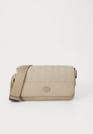 Beige crossover taske lavet af tekstureret syntetisk materiale, med et geometrisk mønster, justerbar rem og en rund logo accent.