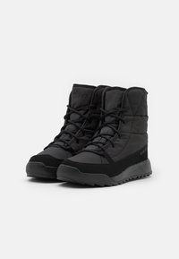 Botas negras impermeables con parte superior acolchada, cordones texturizados y suela resistente. Presenta un logo en el lateral y un acento rojo en el talón.