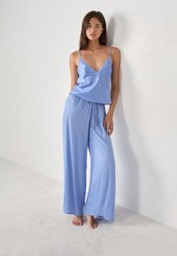 Lichtblauw slaapset bestaande uit een v-hals top met kanten rand en losse, wijde broek met een elastische aantrekband in de taille.