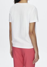 Camiseta blanca de algodón con mangas cortas, cuello redondo y un corte relajado, combinada con pantalones rosa. La tela parece suave y ligera.