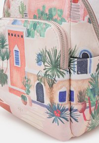 Tessuto rosa morbido con edifici colorati in stile mediterraneo, cactus e piante verdi stampati su un angolo di una borsa con zip.