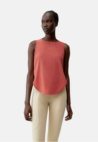 Rode mouwloze top van gladde stof, met een ronde zoom en subtiel logo in het midden, gecombineerd met beige strakke leggings.