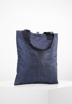 Bolsa de tela azul oscuro con logo negro de Adidas y asas negras, situada sobre una superficie blanca con un fondo blanco.