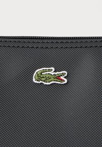 Țesătură texturată neagră cu un logo brodat de crocodil verde, accentuat cu roșu, plasat aproape de marginea superioară.
