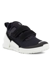 Chaussure de sport noire avec tige en maille, double bande Velcro, semelle rembourrée et accents blancs sur le bout et le talon.