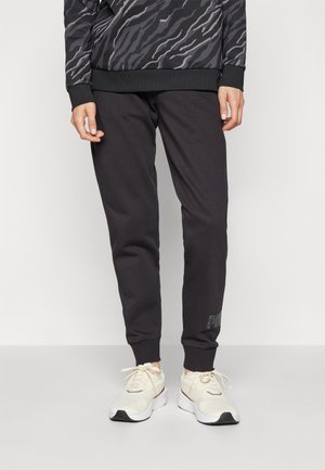 Pantalones deportivos negros con un ajuste relajado, que cuentan con una cintura texturizada, puños acanalados y un sutil logotipo en la pierna izquierda.