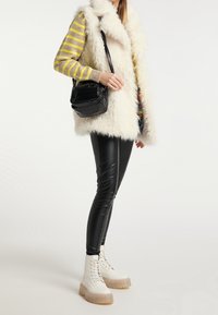 Biała kamizelka z sztucznego futra, pasiasty sweter w żółto-szarym kolorze, czarna błyszcząca torebka, czarne skórzane spodnie oraz białe, masywne buty sznurowane.