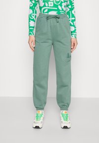 Gröna sweatpants med elastisk midjeband och snörning, med en texturerad logodetalj på vänster lår och avsmalnande muddar.