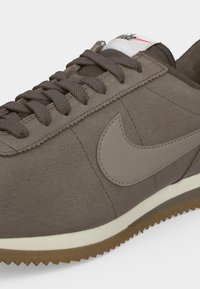 Καφέ σουέντ αθλητικό παπούτσι Nike με ταιριαστά κορδόνια, μπεζ λογότυπο Swoosh και λευκή ενδιάμεση σόλα σε εξωτερική σόλα από καουτσούκ.