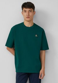 Groen katoenen t-shirt met een ronde hals, korte mouwen en een klein geborduurd ontwerp nabij de borst. Eenvoudig en casual ontwerp.